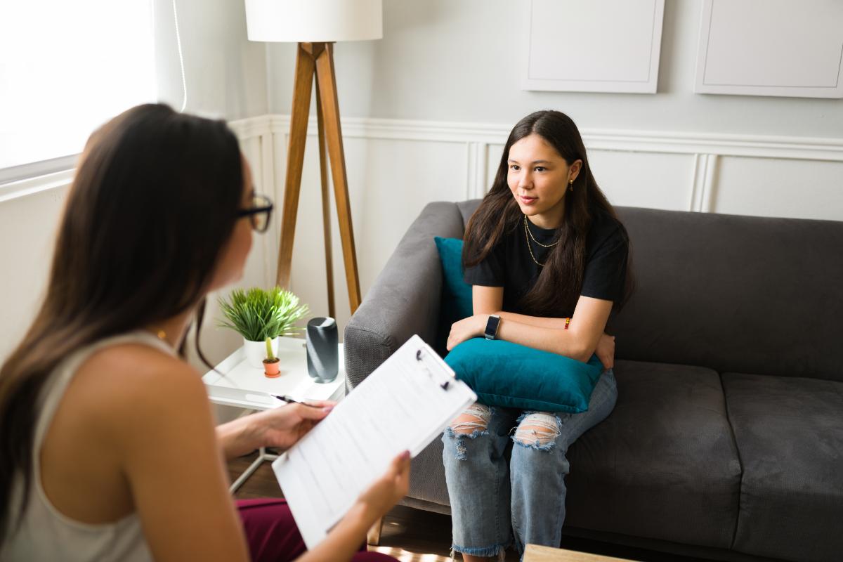 a teen sits on a couch with a therapist during acceptance and commitment therapy for adolescents