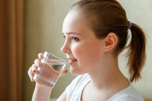 A teen girl is taking anxiety medication. She has a glass of water in her hand.