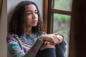 Teen girl with social anxiety gazing out a school window, feeling anxious about social interactions.