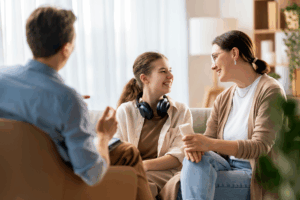 mother and daughter sitting on a couch in therapy smiling and speaking with a counselor