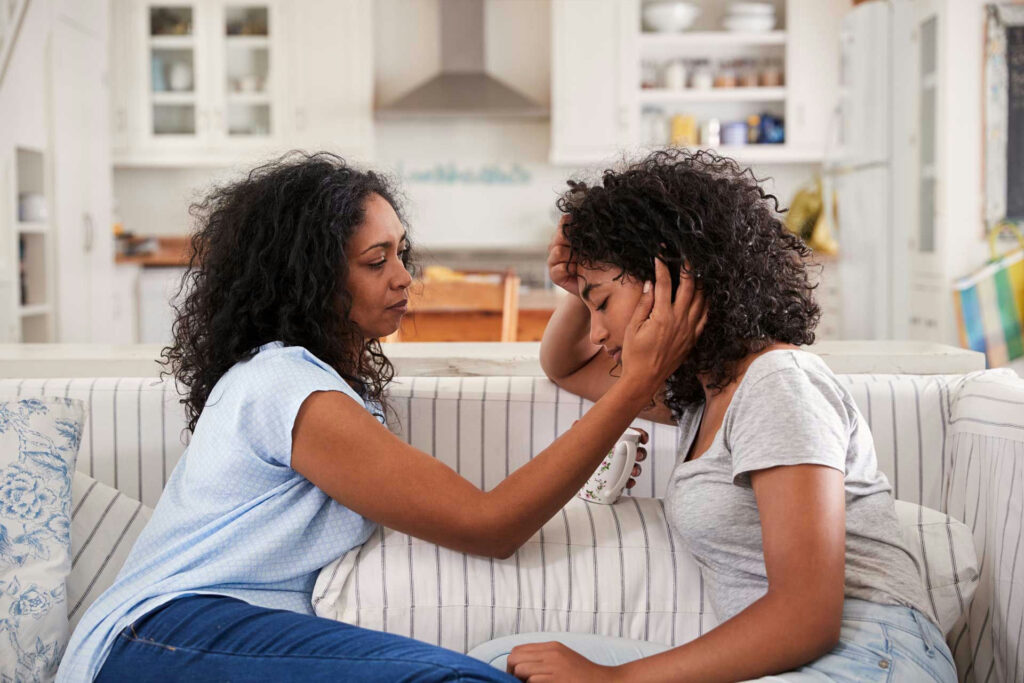 A parent sitting beside their teenager offering gentle support during a difficult moment.