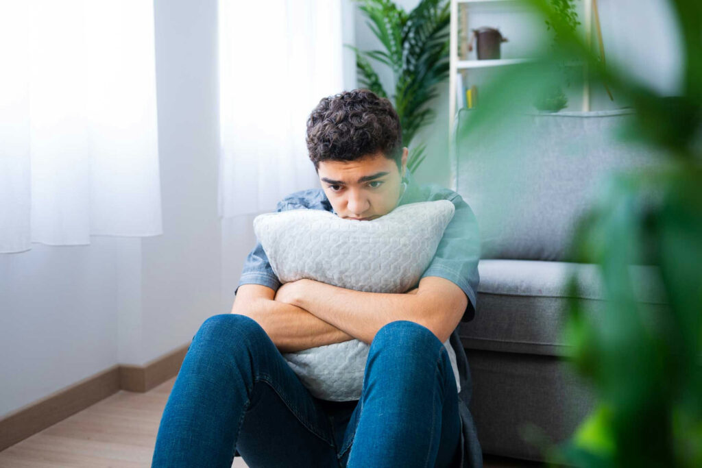 A teenager sitting on the floor, appearing fatigued and withdrawn, illustrating common signs of teen depression.